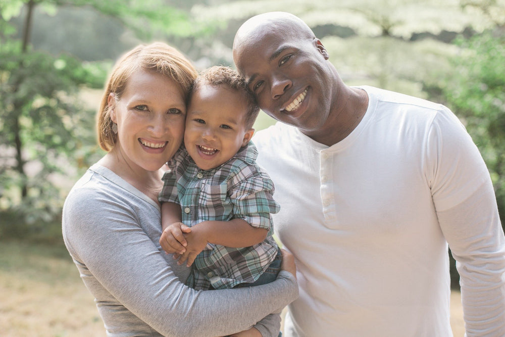 Two parents smiling with their young child outdoors